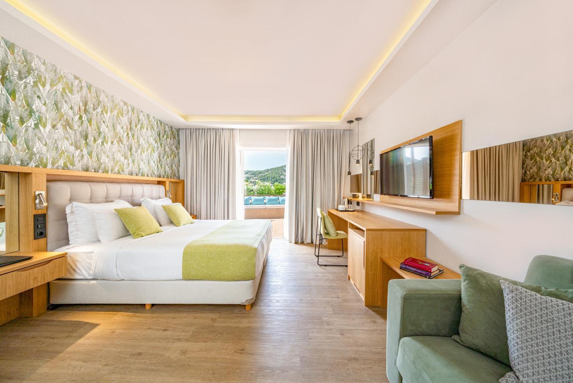 ドルチェ バイ ウインダム アッティカ リビエラ ヴラヴローナ エクステリア 写真 The photo shows a modern hotel room featuring a large bed with white linens and accent pillows in light green. Behind the bed is a decorative wall with floral patterns. On one side of the room, there is a comfortable chair and a small side table. Acr